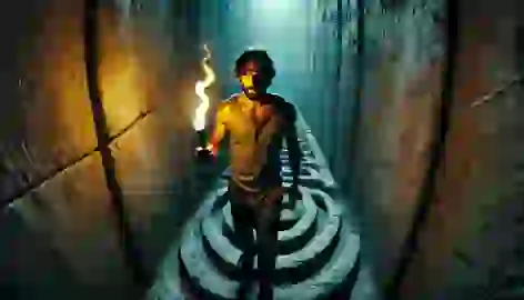 Theseus walks through the dark corridors of the labyrinth, holding a torch and unraveling a ball of thread.